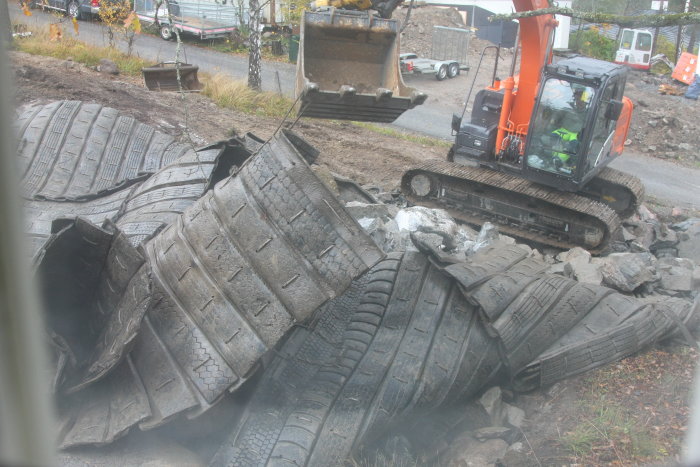 En grävmaskin tar bort gamla bildäck efter en bergssprängning på en byggarbetsplats.