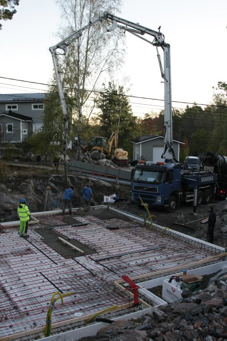 Arbetsplats vid husgrund där gjutning påbörjas med en betongpump och arbetare som övervakar.