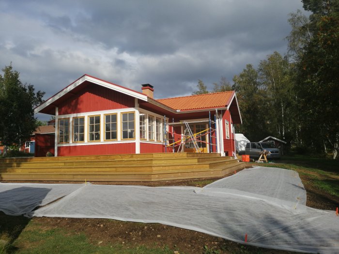 Rödmålat hus med vita fönster och nybyggd veranda under konstruktion.