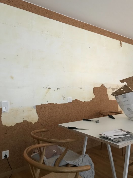 Delvis renoverad vägg med rester av korkplattor och gult lim, skadat gips och renoveringsverktyg.
