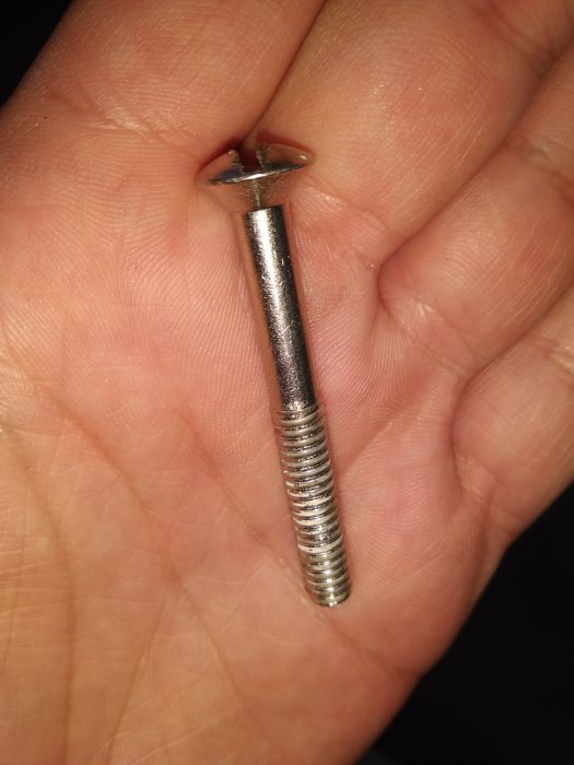 Hand som håller en metallskruv med gängad skaft och plan skalle, tänkt för användning i fönstermontage.