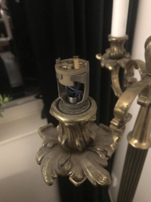 Närbild på en äldre lampans öppna ljushållare och ledningar som behöver renovering.