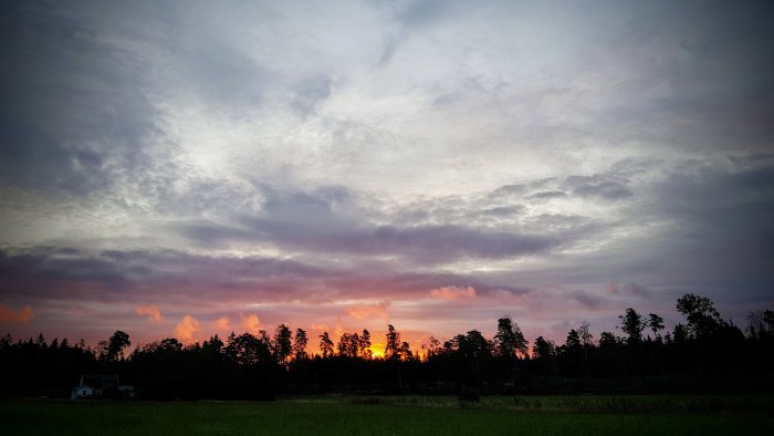 Höstlig solnedgång med livfulla färger över skogsbryn och fält.