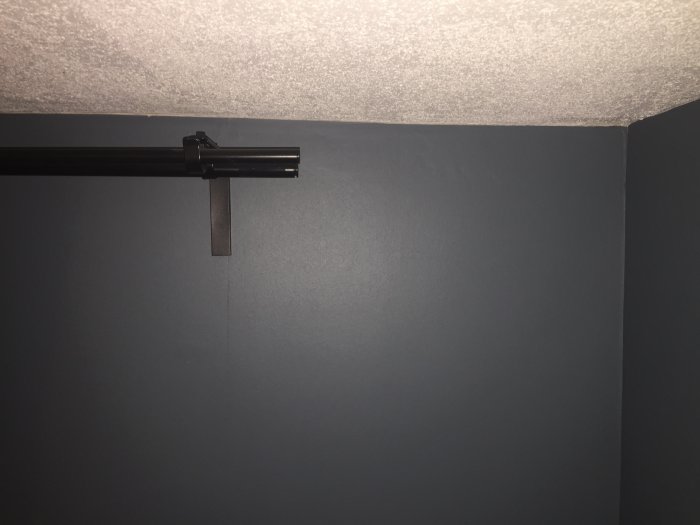 Närbild av mörkgråa vägg med monterad svart gardinstång mot en vit takyta.