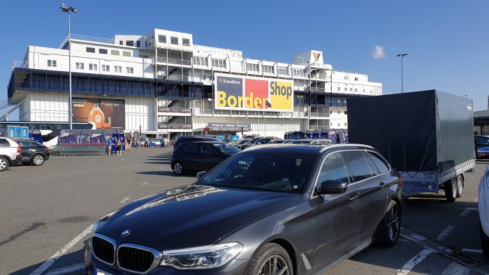 Bil med släpvagn parkerad utanför Scandlines Border Shop under solig himmel.