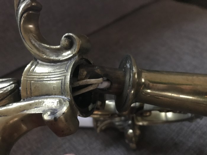 Närbild av en patinerad mässingsljuskronas detalj med synlig ljushållare och dekorativa element.