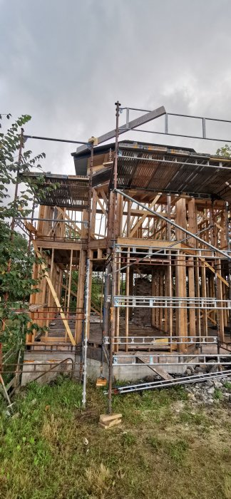 Delvis byggt trähus med ställningar runt omkring under grå molnig himmel.