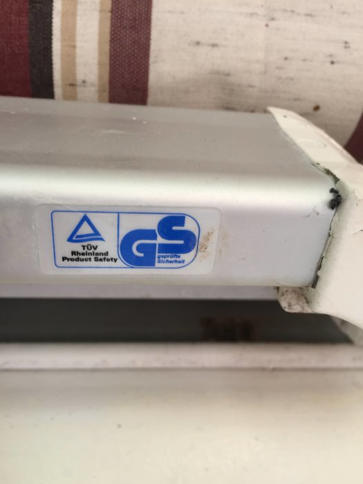 Närbild på en TÜV Rheinland Product Safety och GS-säkerhetsdekal på en vit apparat.