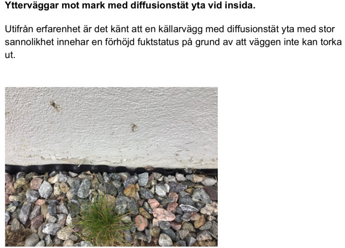 Källarvägg med tecken på fukt och vit diffusionsresistent färg nära mark med grus.