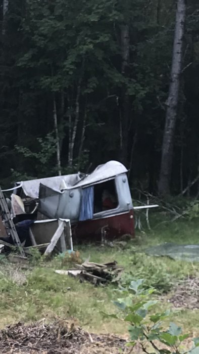 Övergiven vagn på en röjd yta med skog i bakgrunden, nedfallna grenar och skräp i förgrunden.