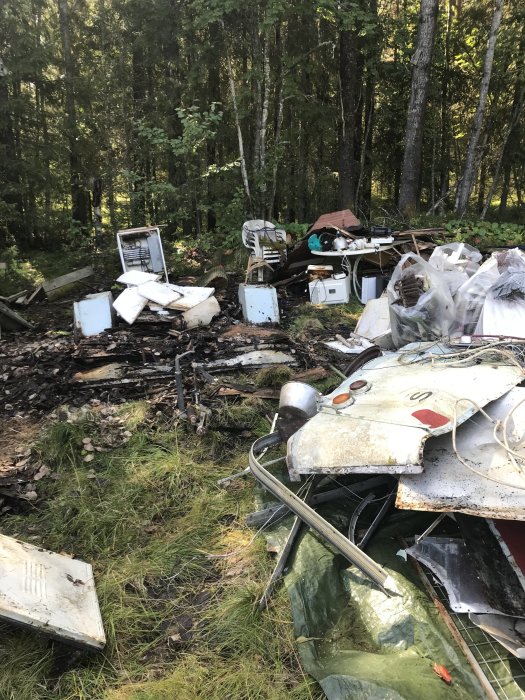 En hög med diverse skräp och byggavfall, inklusive metall, frigolit och trasig elektronik, i en skogsglänta.
