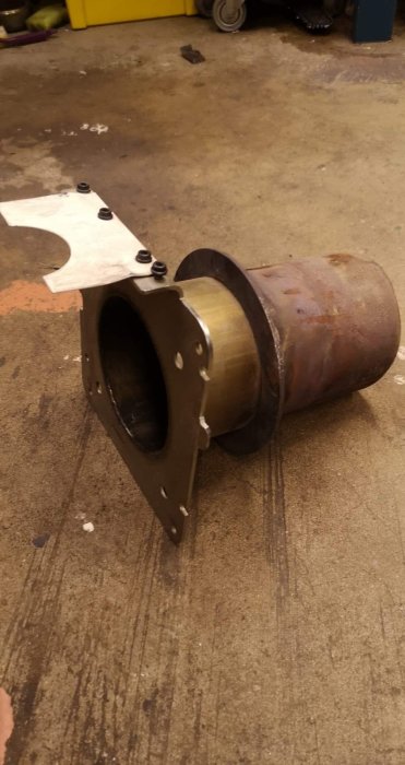 Rostig vedpanna stos med skadad fläns och skruvhål på betonggolv.