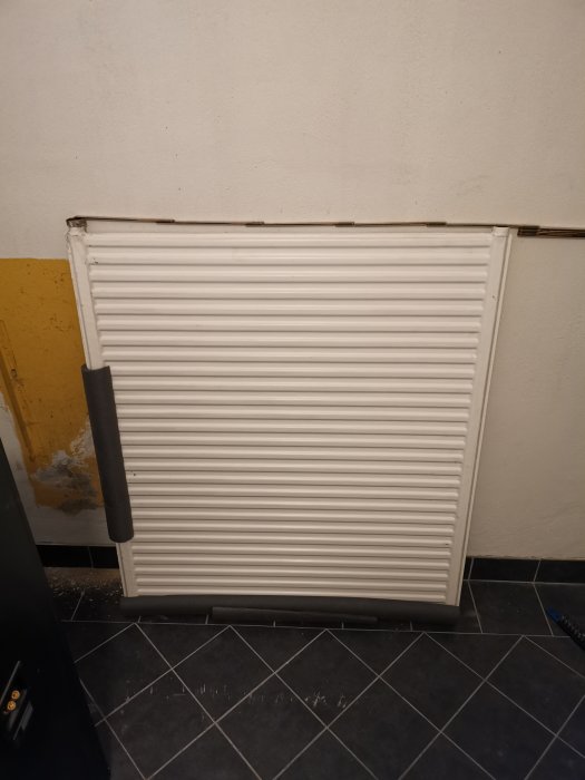 Gammalt element i vitt står mot en vägg, i behov av koppling till radiatorledningar.