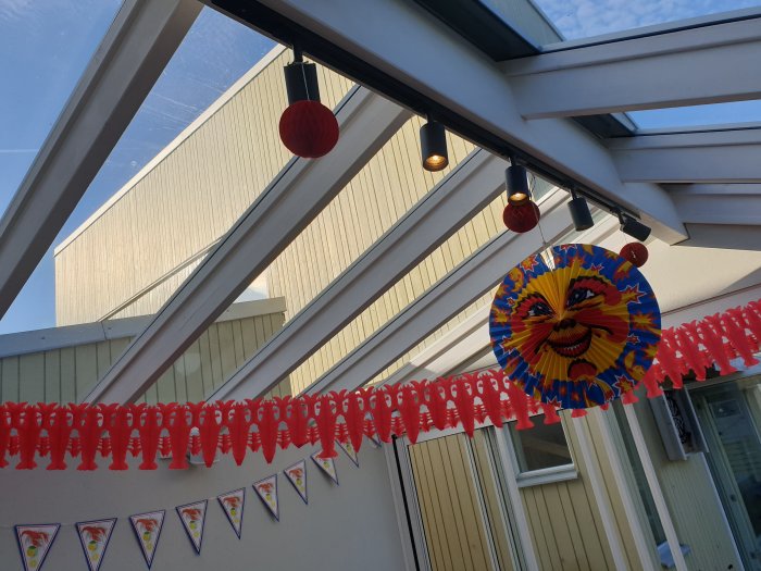 Färdigt rum med tak av glas, dekorerat med färgglada lampor, en sol-utsmyckning och festliga girlanger.