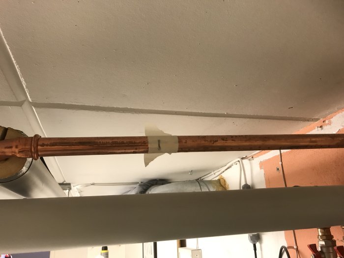 Kopparrör med tejpmarkerad del för presskopplingsinstallation mot ett tak.