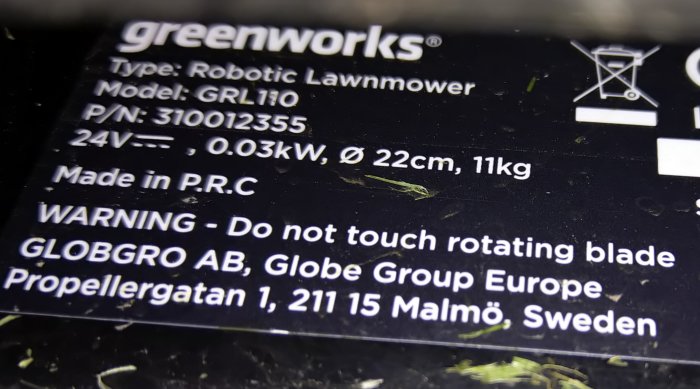 Närgränsad bild av en etikett på en Greenworks robotgräsklippare som visar modellinfo och varningstexter.
