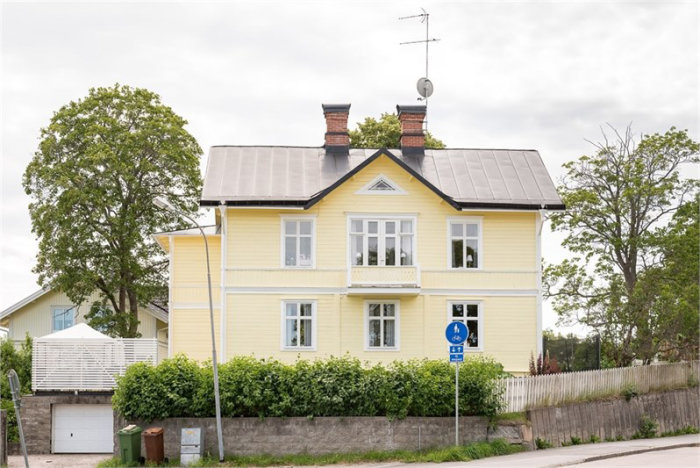 Gult äldre charmigt hus med snickarglädje och solpaneler på taket.