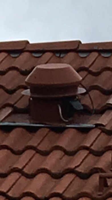 Fläkt utan skorsten på tak med tegelpannor, omgiven av andra hus med skorstenar.