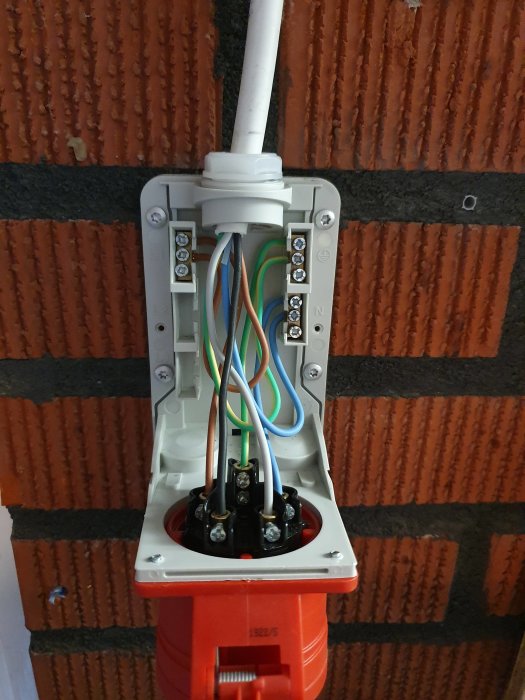 Eluttag med öppen förläggning som visar elsladdar anslutna till plintar och 1-fas uttag monterat på tegelvägg.