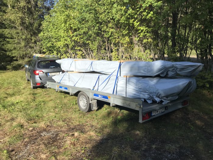 Bil med släp överlastat med byggmaterial för kojbygge parkerad utomhus.