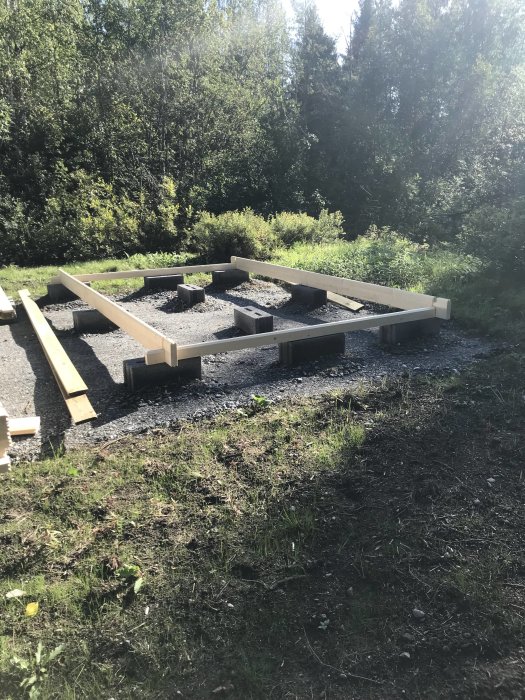 Grundstommen för en koja med träbalkar på betongblock i grönskande natur.