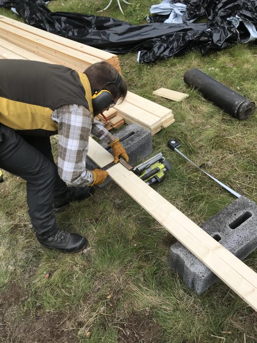 Person i arbetskläder som kapar en träbräda med cirkelsåg utomhus.