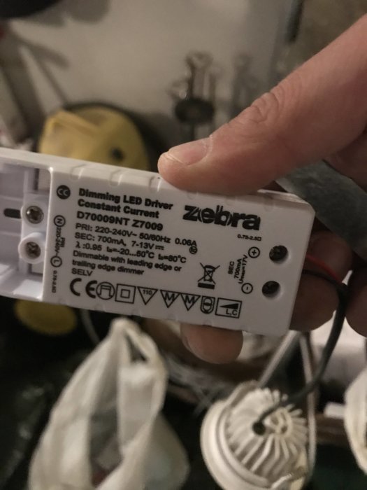 Hand håller en dimbar LED-driver från Ziebra med teknisk info och säkerhetssymboler.