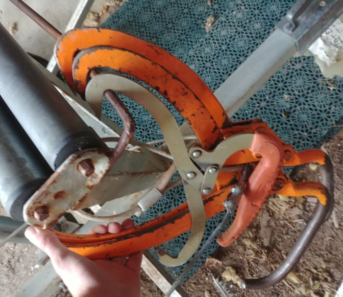 En handhållen vedklipp med orange griparmar och metallkomponenter för klyvning av vedstockar.