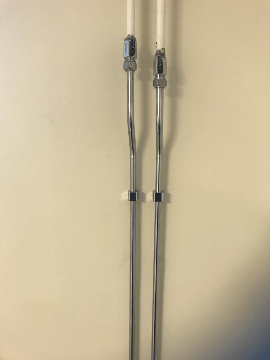 Två kopplade kromade rörledningar med S-bockar för element, monterade på en vägg.
