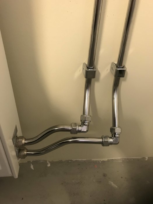 Kromade vattenrör anslutna till vägg med S-bock och väggfästen vid installation av element.