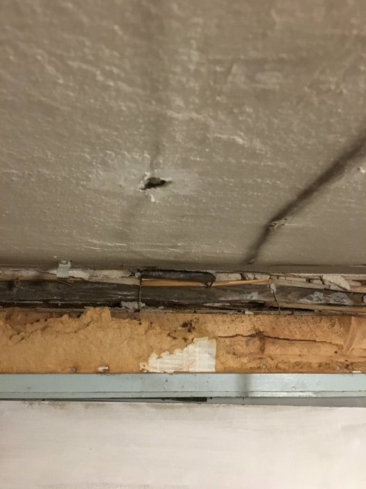 Kuva kellarikerroksesta, jossa näkyy betoninen kattopinta vauriolla ja eristeitä alapuolella. Rakenteessa on tummia ja epätasaisia kohtia.