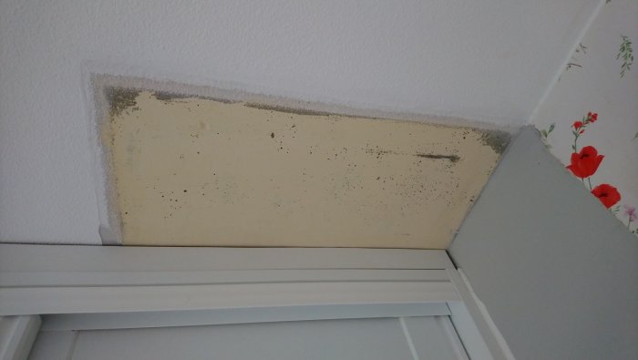 Ospacklad yta på tak med synlig grundfärg och vägg med blomster tapet, behov av renovering.