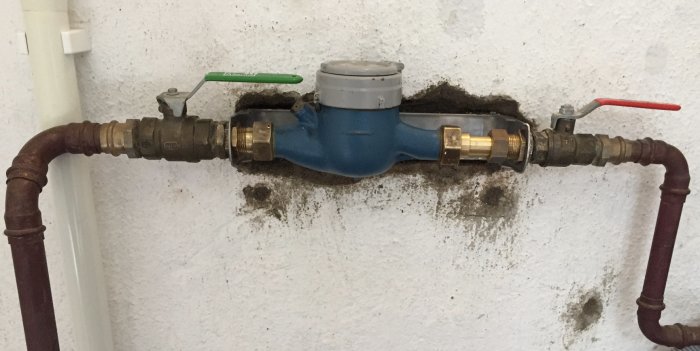 Nyinstallerad konsol med vattenmätare och rör på vägg, tecken på fuktläckage runt anslutningen.