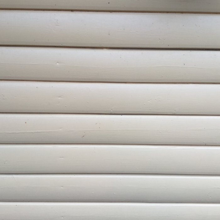 Välvda vita träpaneler som behöver bytas ut vid renovering av ett uthus.