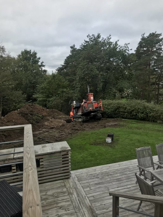 Arbetsfordon på bakgård med uppbörd jord, synlig från träaltan med utemöbler.