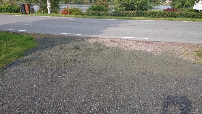 En hög med grus vid sidan av en landsväg, med gräs och träd i bakgrunden.