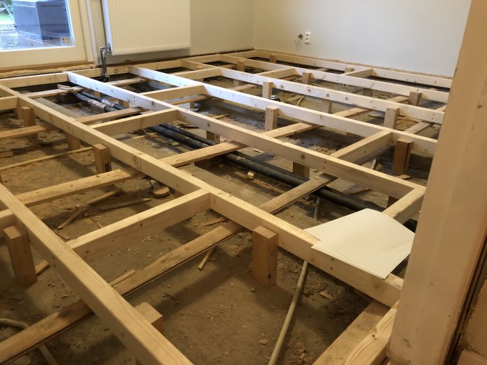 Nyinstallerade golvreglar av trä i olika längder med stöttor i ett rum under renovering.