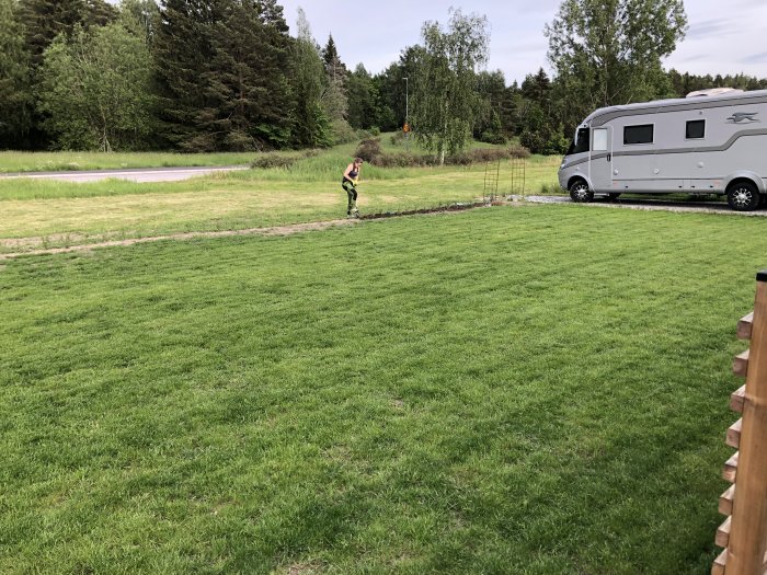 Välskött gräsmatta med husvagn i bakgrunden och person i kanten på en klar dag.