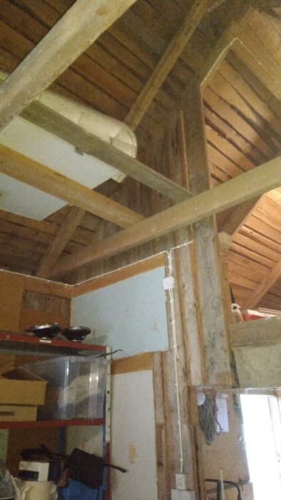 Träbalk i taket i ett loft, ovanför en trappa där person ofta slår i huvudet.