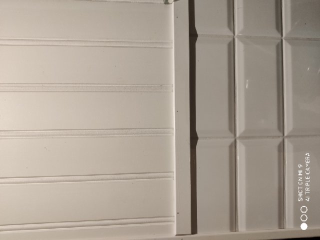 Vägg med vit panel ovanför och vit kakel nedanför, ingen synlig elutrustning.
