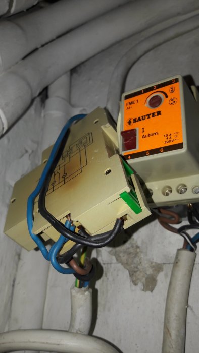 En gammal trappautomat med märkningen "Sauter" och elanslutningar mot en vägg.