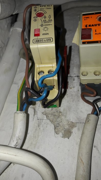 Trappautomat av märket Landis+Gyr med inställningsratt och anslutna elledningar mot vägg.