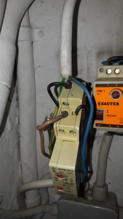 En trappautomat märkt "Landis & Gyr KPE 10.1" med anslutna elektriska sladdar vid en vägg.