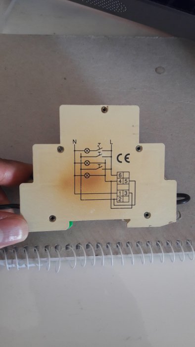 Gammal trappautomat med skissat kopplingsschema, märkt med CE, hållen framför en anteckningsbok.