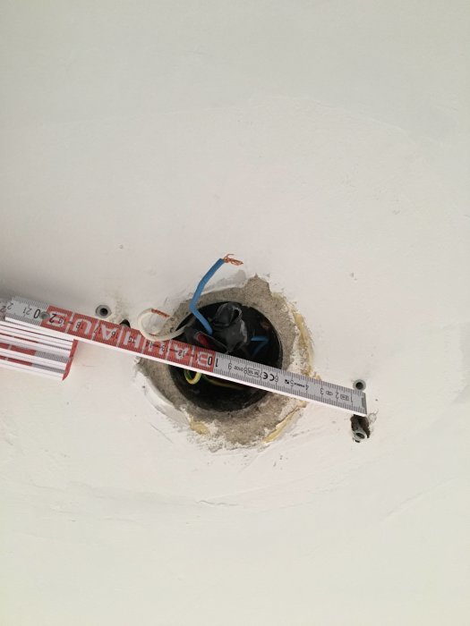 Hål i tak med lösa kablar och svart plast, mätsticka visar dimensioner.