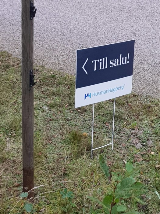 Till salu"-skylt från HusmanHagberg placerad i gräsmark.