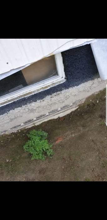 Husgrund efter dränering med synliga isoleringsmaterial och utan täcklist vid källarfönster.