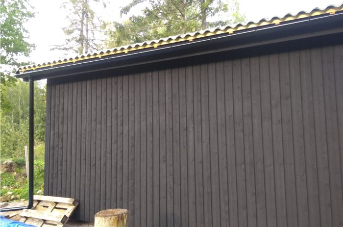 Nyinstallerad hängränna och stuprör på en grå byggnads långsida med nyligen uppsatt ytterpanel.