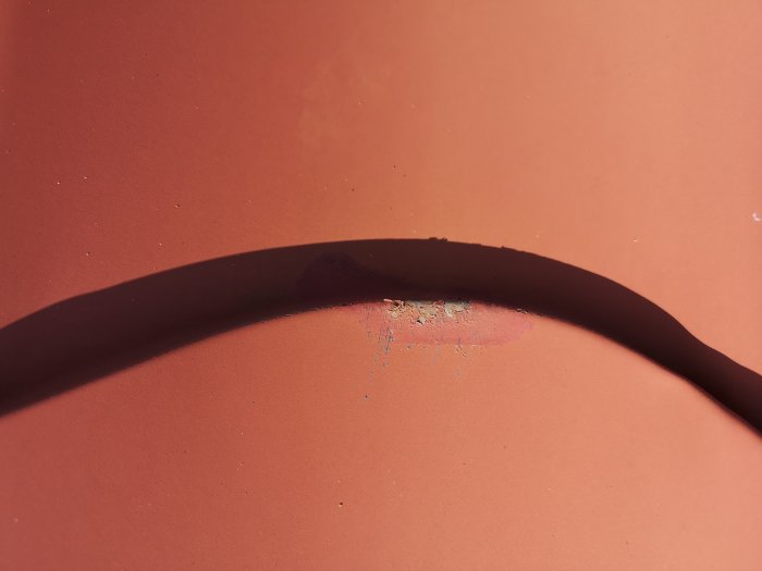 Skugga av böjd kabel över en orange yta med skada i mitten.
