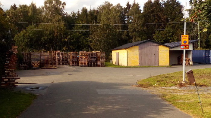 Industriområde med högar av EU-pallar och gula lagerbyggnader, nära bostadsfastighet.